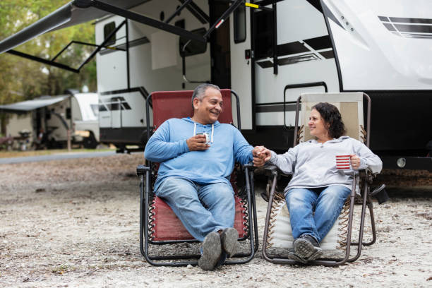 Multiracial couple sitting in chairs by camper in RV park A mature multiracial couple sitting together in chairs by a camper trailer in an RV park, drinking coffee. He is Hispanic and she is Middle Eastern and Caucasian. They are conversing, smiling, looking at each other, and holding hands. body positive couple stock pictures, royalty-free photos & images