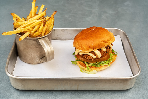 Classic fried chicken burger with vegetables and fried potatoes in a vintage mug and metal tray. High quality photo