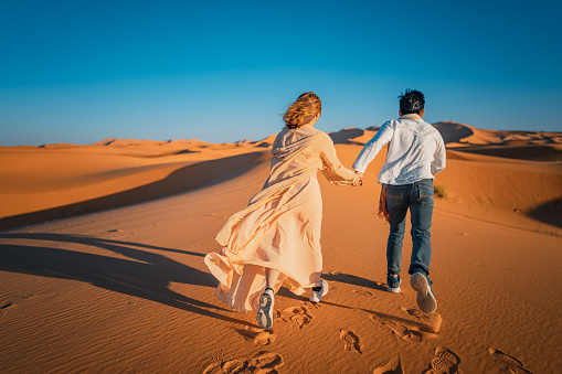 Rear view Portrait Asian Chinese Couple running in Morocco Sahara Desert