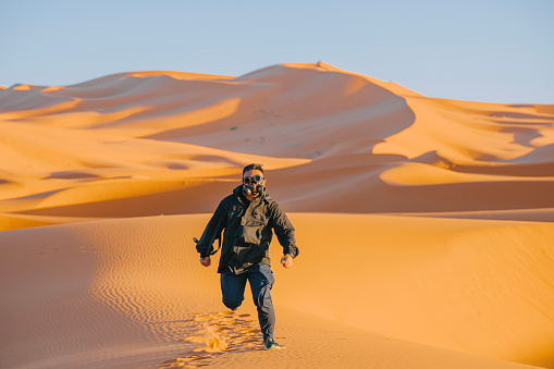 Desert adventure. Young man with backpack walking on sand dune. Abu Dhabi, United Arab Emirates