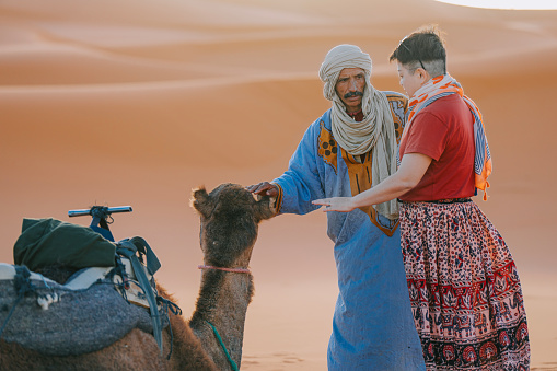 Moroccan Tour Guide showing camel to Asian Chinese female tourist in Sahara Desert