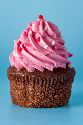 cupcake with strawberry cream and sprinkle of hearts on blue background macro close up vertical