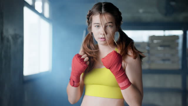 Boxing movements are being practiced by a young woman of white race in a boxing facility.