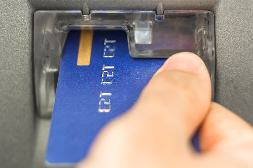 Hand inserting ATM card into bank machine to withdraw money