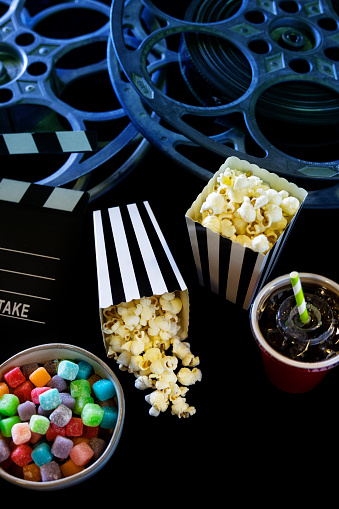 This is a conceptual photo relating to watching a movie. There are two old retro movie reels on a black background and two black and white striped bags of popcorn.