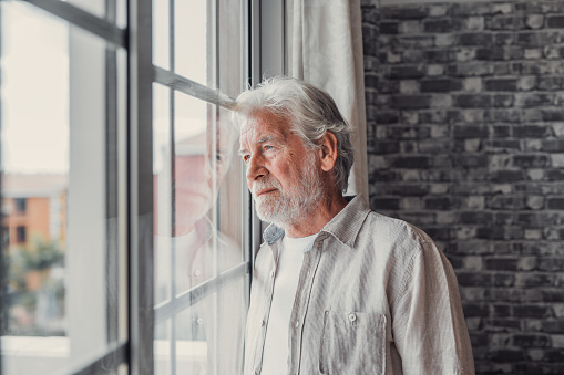 Pensive elderly mature senior man in eyeglasses looking in distance out of window, thinking of personal problems. Lost in thoughts elderly middle aged grandfather suffering from loneliness, copy space