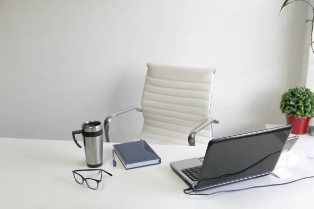White empty office with comfortable chair, plants, ready to start the working day on laptop, cell phone