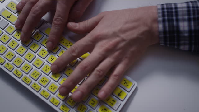 Close-up: A man uses a keyboard with braille.A blind man is typing words on the buttons with hands