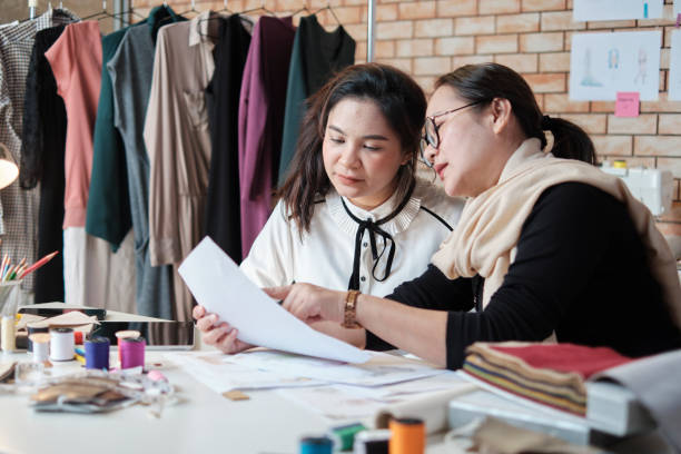 Asian female and teen tailor work with design sketch drawing and sewing thread. stock photo