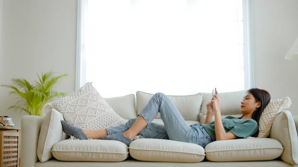 istock Happy young asian woman relaxing at home. Female is lying down on sofa and using mobile smartphone 1463971145
