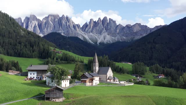 Small mountain village with church under Dolomites mountains in Italy, Val Di Funes aerial. St. Magdalena.
