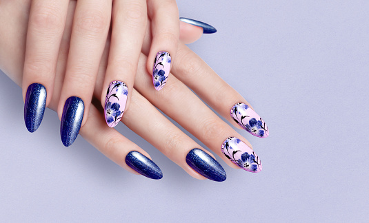 Hand of the girl. Blue manicure. Long colored acrylic nails. Female manicure and floral patterns.