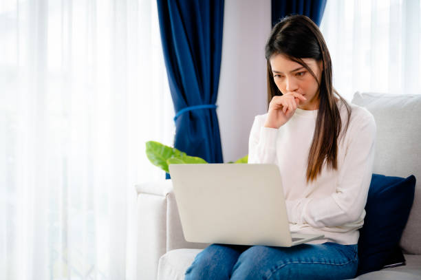 Young asian woman working on computer laptop on couch in living room at home stock photo