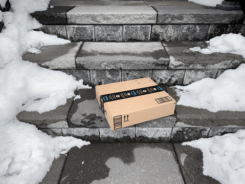 Toronto, ON, Canada - January 27, 2023: A flat Amazon shipping box delivered at doorstep with snow on the sides.