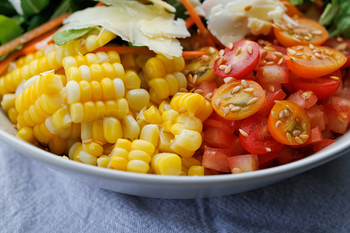 A multi-coloured healthy salad bowl with assorted fresh fruits and vegetables, lettuce, tomatoes, carrot, corn and cheese close-up
