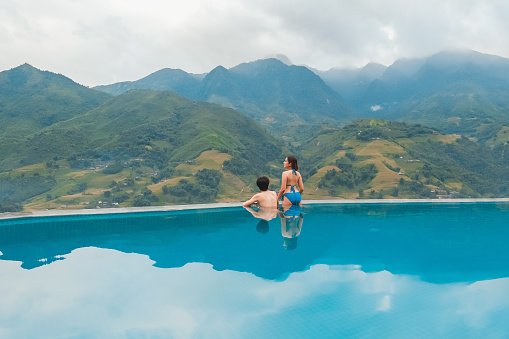 Young woman relaxes on edge of outdoor swimming pool in tropical jungle