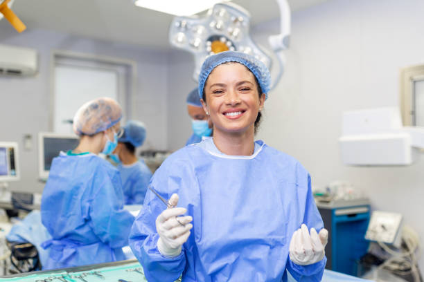 患者に取り組む準備ができて、手術室に立っている幸せな女性外科医の肖像画。手術劇場で外科用ユニフォームを着た女性医療従事者。 - scrubs surgeon standing uniform ストックフォトと画像