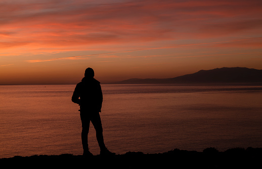 Silhouette of adult man looking at sea view during sunset