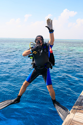 Middle aged Athletes  handsome men scuba divers ready for scuba diving,  jumping in   Beautiful tropical blue sea, coral reef  in the background. Water sports.