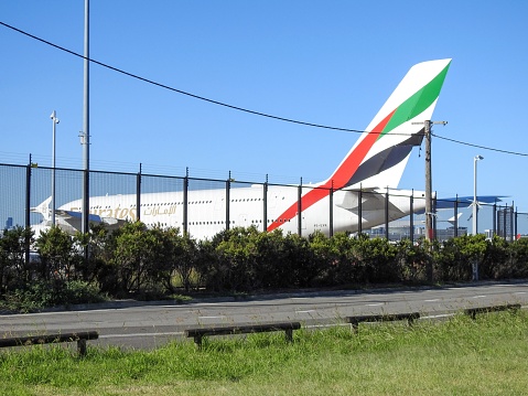 An Emirates Airbus A380 parked at Sydney Kingsford-Smith Airport.  This plane, registration number A6-EVR, arrived earlier in the day from Dubai as flight EK412 and is parked away from the terminal, waiting for the return flight at 10pm.  A warning sign on the fence indicates it is electrified.  In the distance are office and residential towers.  This image was taken from Kyeemagh Avenue, Kyeemagh on a sunny afternoon on 5 February 2023.