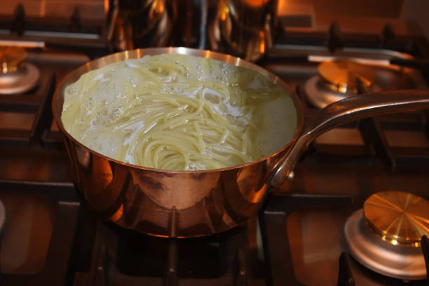 Spaghetti being cooked in a copper pan filled with boiling water
