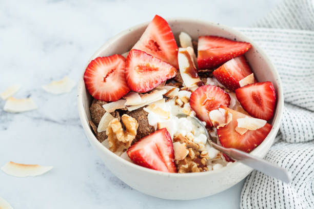Cottage cheese bowl with strawberries, cereal flakes, coconut, nuts and syrup, marble background. stock photo