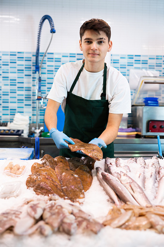 Responsive shop assistant in work apron holding sole in fish shop with large stock