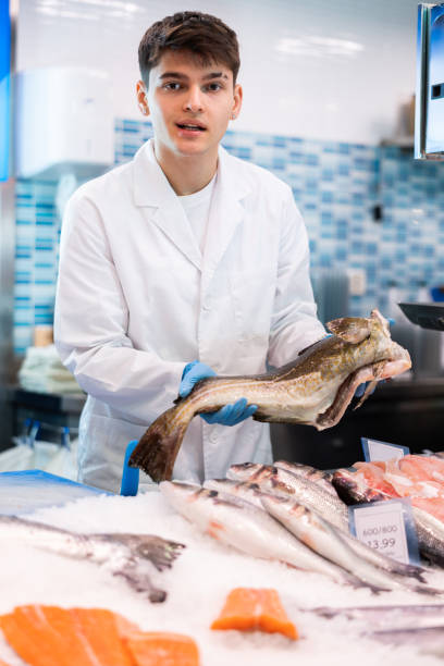istock Portrait of man offering fresh fish atlantic cod at seafood shop 1464022887
