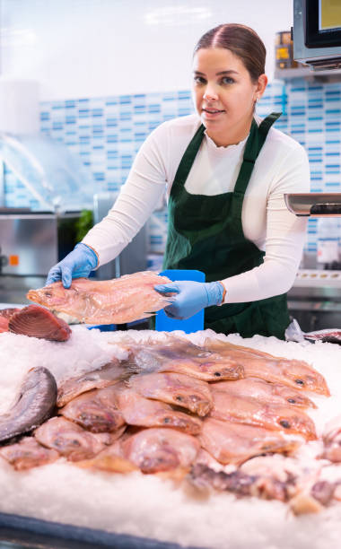 istock Smiling salesclerk demonstrating scaldfish in fish store 1464023115