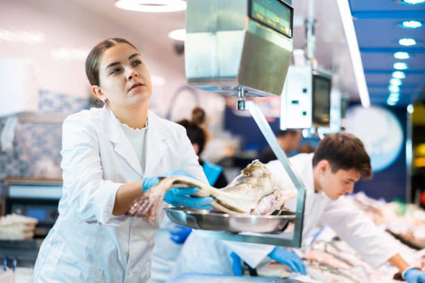 istock Skilful shop assistant weighing cod fish on scales in fish store 1464023161