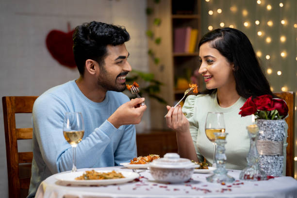 Happy smiling young couple having dinner while talking eachother during candle light dinner at home - concept of romantic moment, dating and togetherness Happy smiling young couple having dinner while talking eachother during candle light dinner at home - concept of romantic moment, dating and togetherness. indian dinner stock pictures, royalty-free photos & images