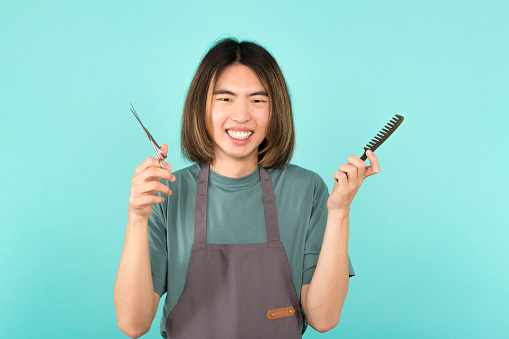 Studio portrait with blue background of a cool asian hairdresser looking and smiling at the camera