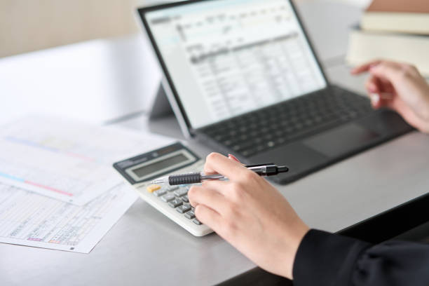 Asian woman entering journal entries in accounting software stock photo