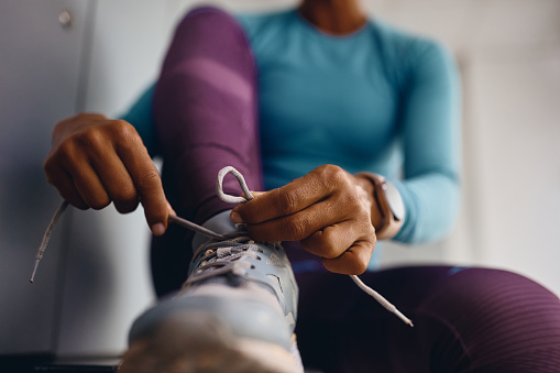 Close up of African American athletic woman tying shoelace on sneakers while preparing for workout at health club.
