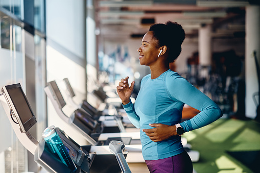 Happy African American athlete jogging on treadmill during her sports training in a gym.