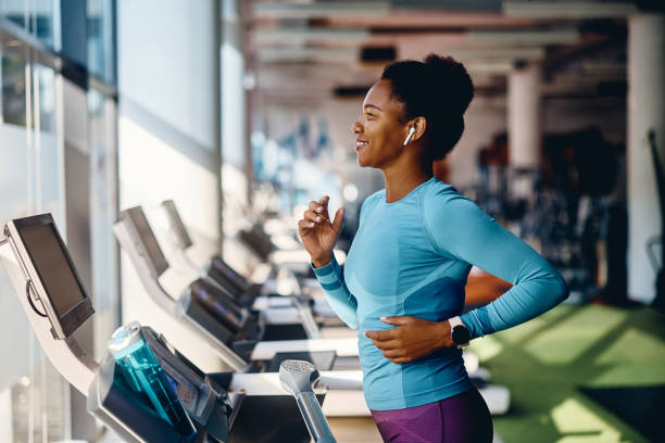 Happy black athletic woman running on treadmill while working out in gym. stock photo