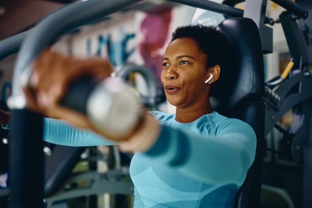 Black sportswoman doing chest exercises on machine while working out in gym. stock photo