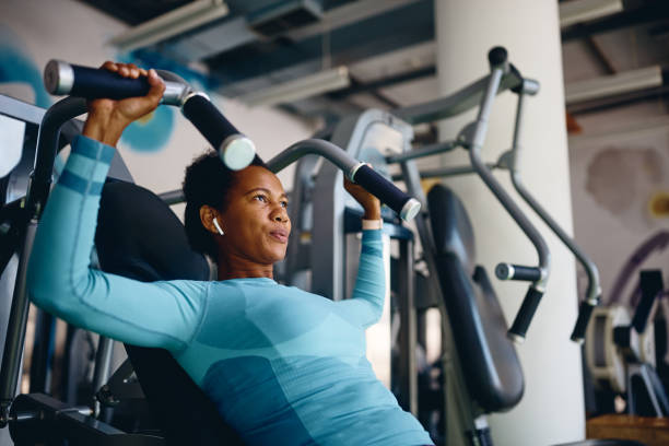 donna atletica afroamericana che utilizza la macchina per esercizi durante l'allenamento sportivo nel centro benessere. - macchina per allenamento foto e immagini stock