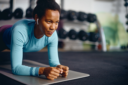 African American athlete in plank pose exercising her strength during sports training in gym.