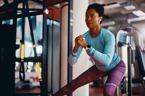 African American athletic woman practicing side lunges while working out in gym.