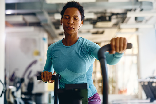 African American athletic woman exercising on stationary bike in gym.
