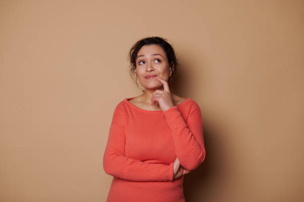 istock Charming middle-aged woman, thoughtfully looking aside, holding finger near her lips while reasoning on beige background 1464038423