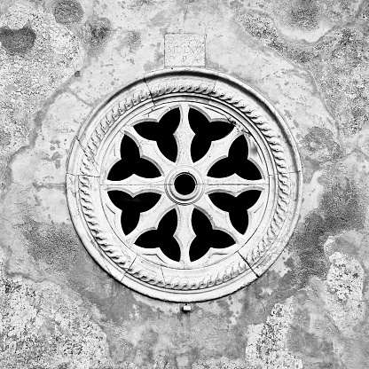 Medieval italian stone rose window against a plaster wall - Italy - Toned image