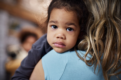 Sad African American girl being consoled by her adopted mother at home.