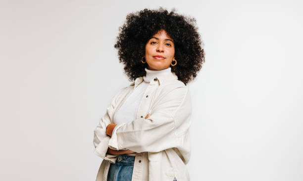 Self-confident woman with an Afro hairstyle standing in a studio Self-confident woman with an Afro hairstyle looking at the camera while standing against a studio background. Attractive young woman of colour wearing her curly hair with pride. woman arms folded stock pictures, royalty-free photos & images