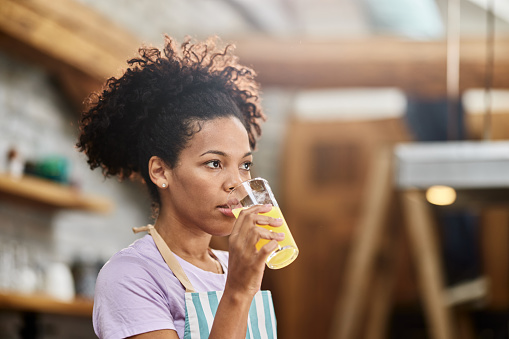 African American woman drinking fresh orange juice in the kitchen.