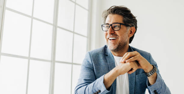 Business man looking outside the window in an office Business man looking outside the window in an office. Senior business man thinking about work while sitting at his desk in a suit. business people stock pictures, royalty-free photos & images