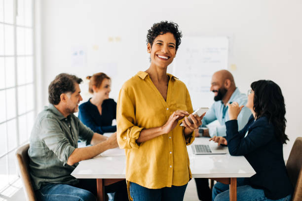 business woman standing in a boardroom and using a smart phone - cheerful happiness men women imagens e fotografias de stock