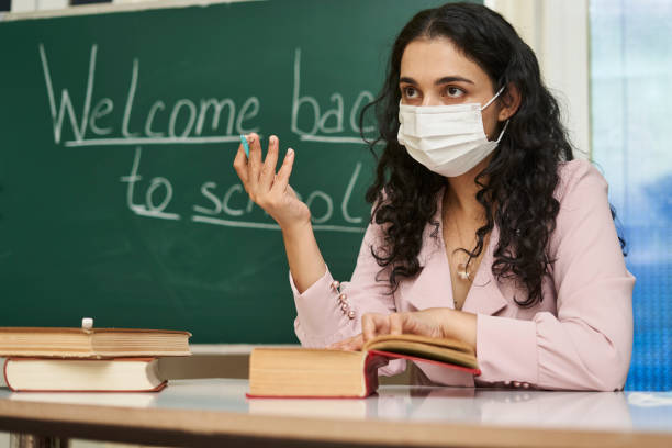 istock Multi-racial female teacher with a facemask explaining a lesson in front of the blackboard 1464050764