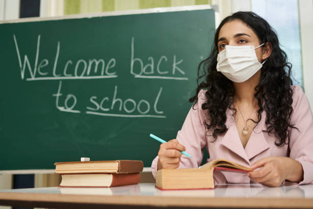 istock Multi-racial female teacher with a facemask explaining a lesson in front of the blackboard 1464050795
